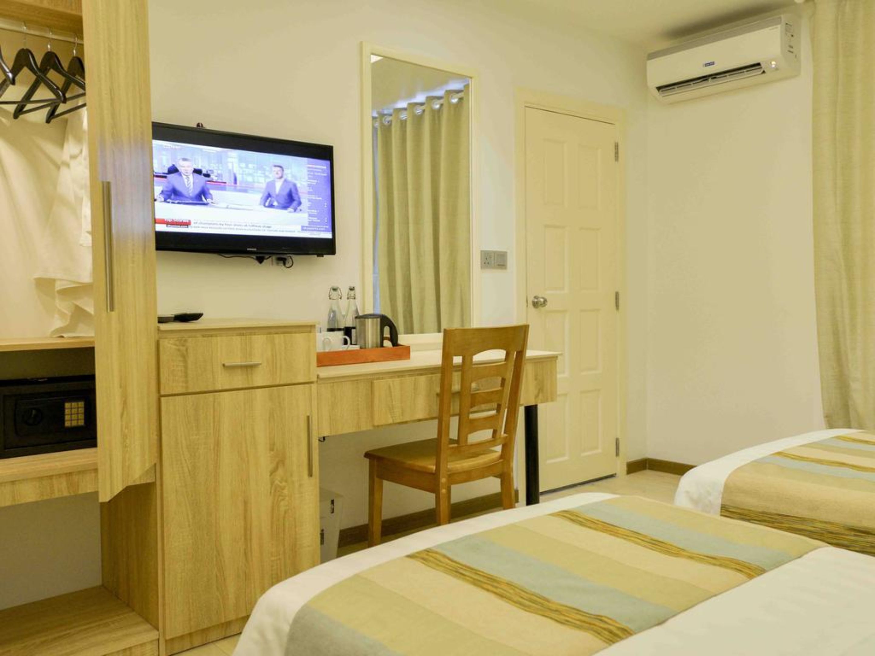 A hotel room with a TV on the wall, a wooden desk, a chair, and two beds with striped bedding.