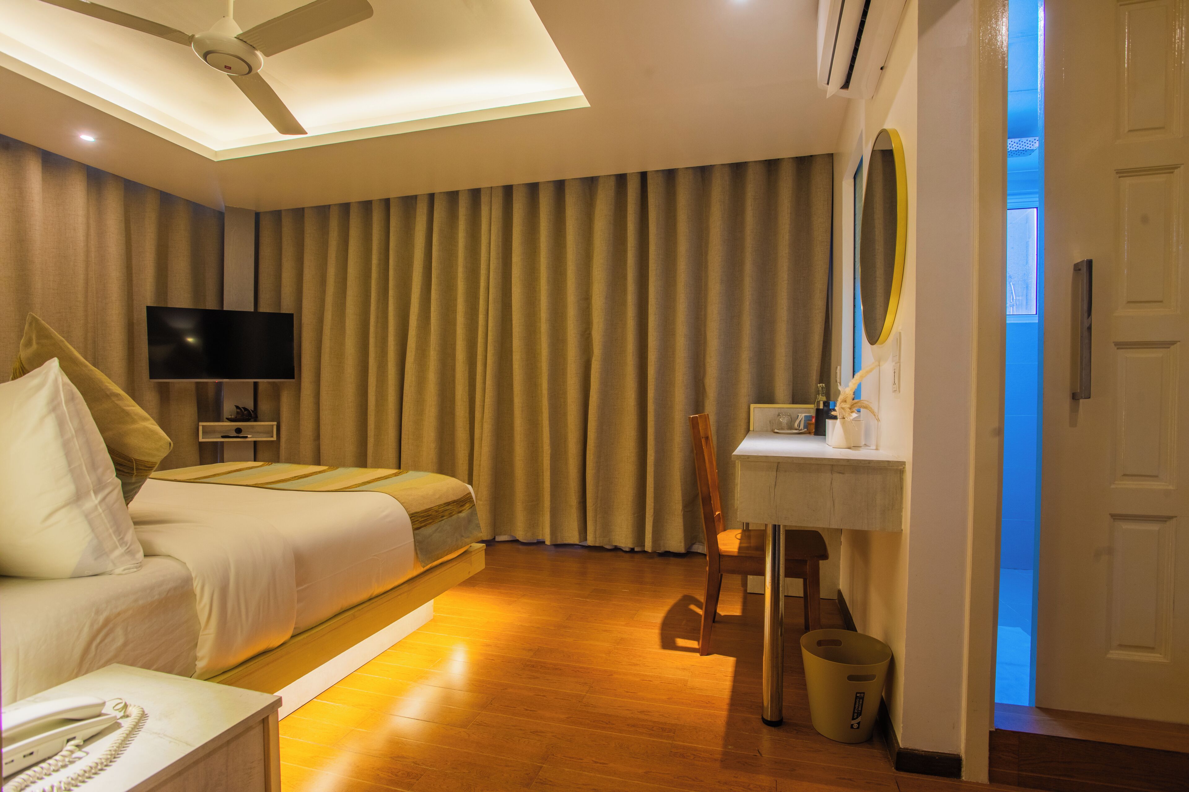 Een hotelkamer met een bed, een bureau, een stoel, een televisietoestel en een plafondventilator.