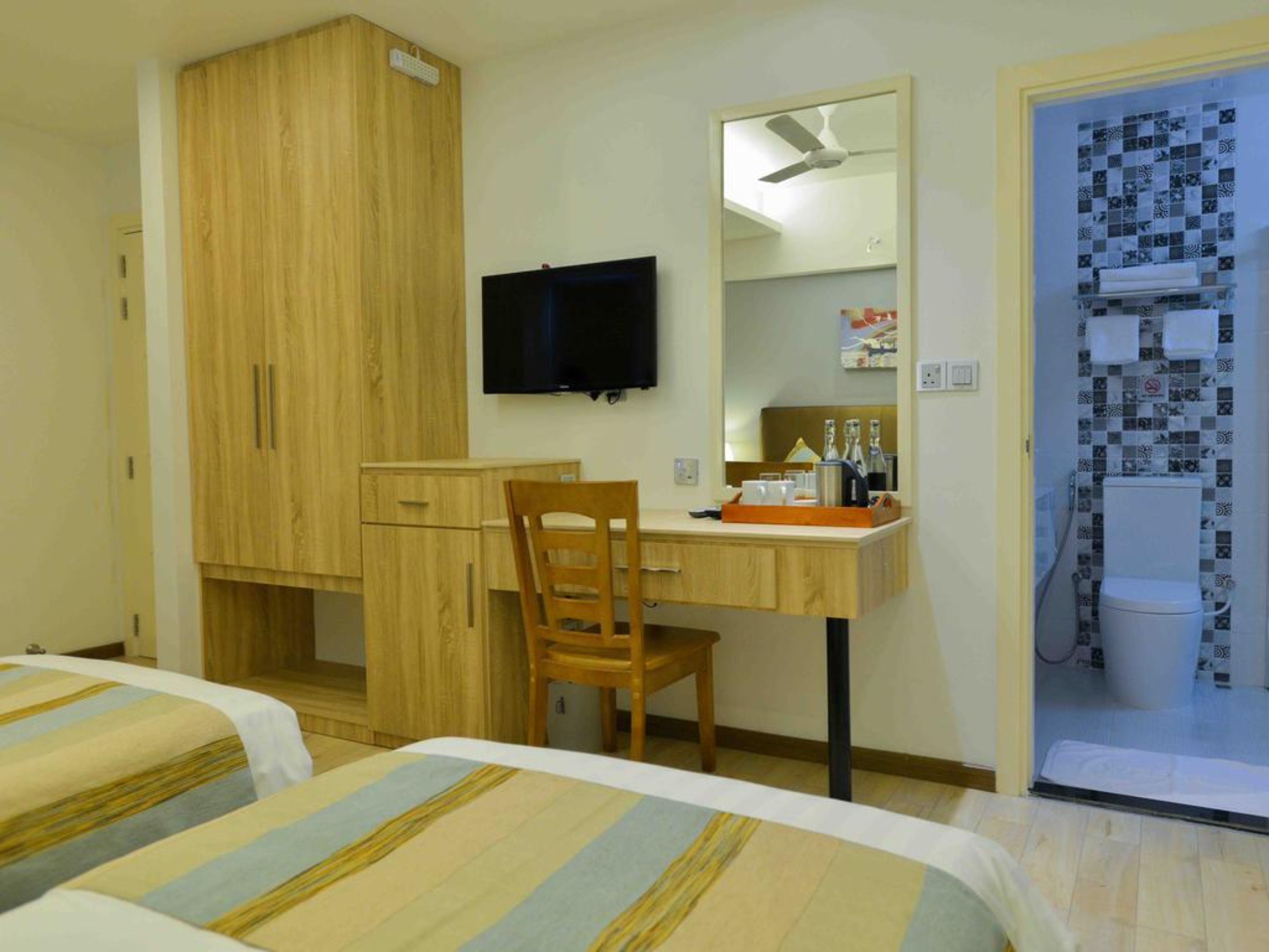 A hotel room with a wooden wardrobe, a desk with a chair, a television, and a bathroom visible through an open door.
