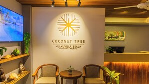 A reception area with a TV, reception desk, two chairs, and a wall with a logo and text. - Coconut Tree Hulhuvilla Beach (Hulhumalé)