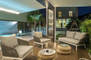 A modern outdoor lounge area with wicker furniture, a glass railing, and a view of a building at night. - Hotel Olimpia (Bellaria-Igea Marina)
