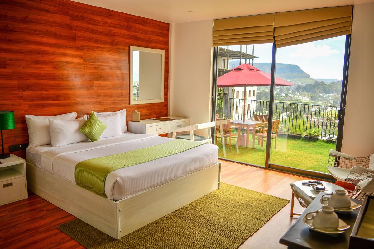 Habitación de hotel con una cama grande, un escritorio, una silla y un balcón con vistas al paisaje.