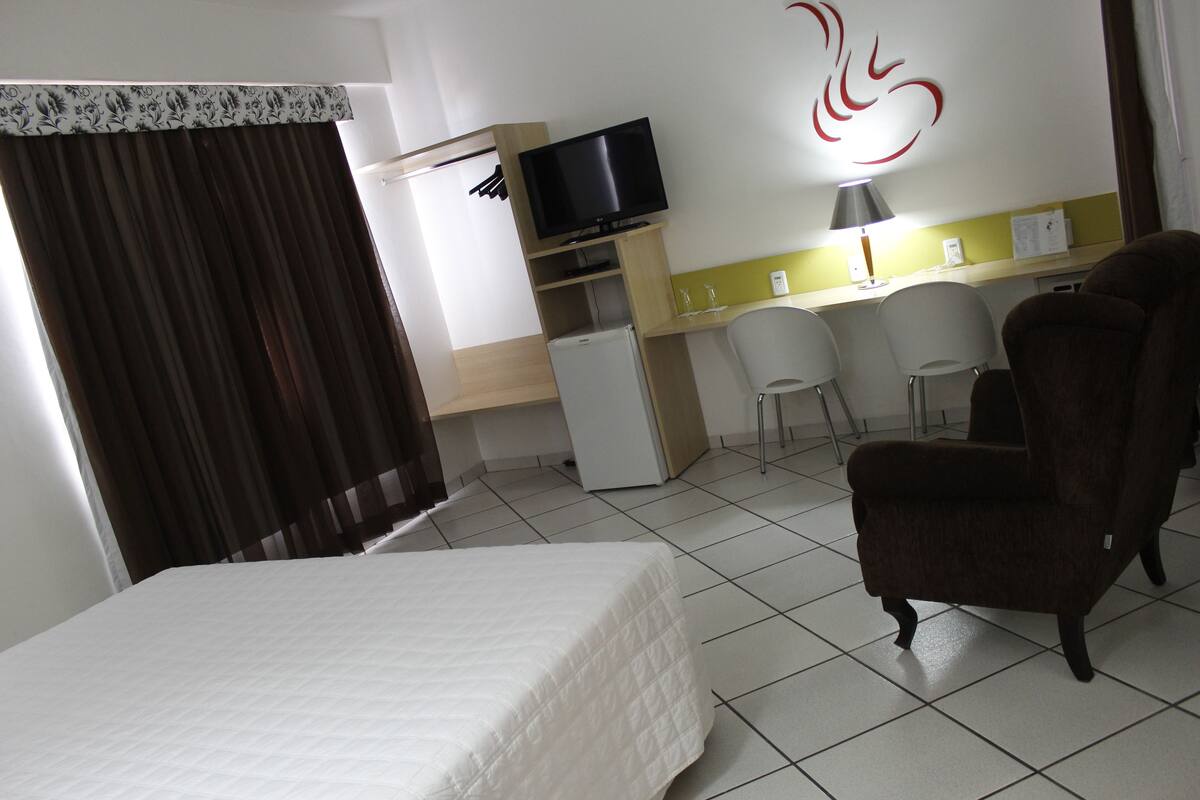 Una habitación de hotel con una cama, un escritorio con computadora, televisión y una silla.