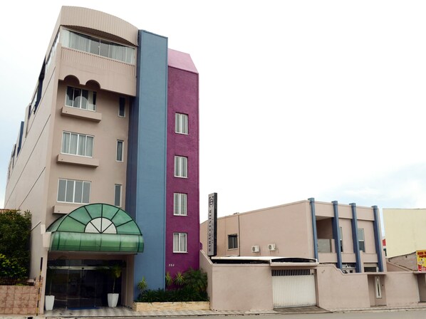 Un hotel de varios pisos con un toldo de entrada verde, fachada púrpura y azul, y techo plano.