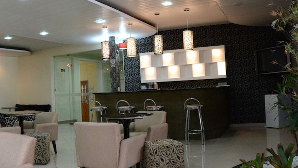 A modern hotel lobby with a reception desk, seating area with chairs and ottomans, patterned wall decor, and pendant lighting. - Barao Center Hotel (Santarém)