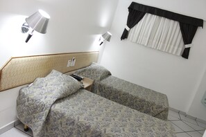 Habitación de hotel con dos camas, cabeceros, lámparas de noche, una ventana con cortinas y un teléfono en la pared.