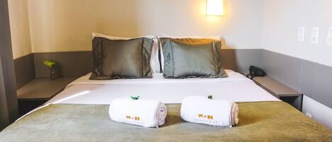 Une chambre d’hôtel avec un lit, deux oreillers, une table de chevet avec une lampe, un téléphone et deux serviettes sur le lit.