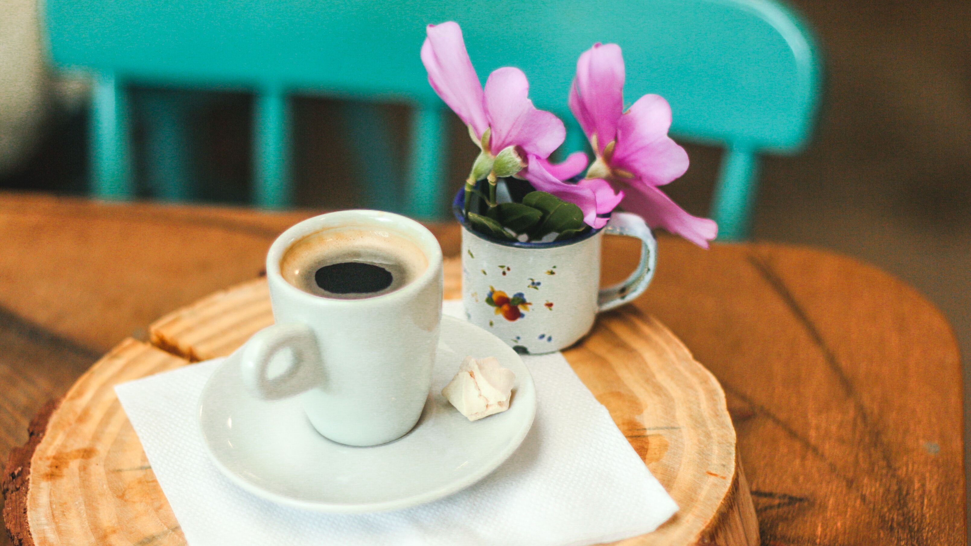 Een witte koffiebeker op een schoteltje, met een mok met bloemen erop, geplaatst op een houten tafel met een servet.