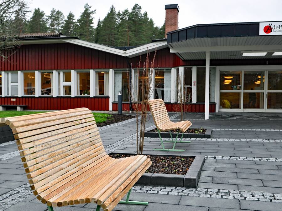 Un bâtiment à la façade rouge, sur lequel on peut lire l’inscription « Aðelfors Húsavellir ». Deux bancs en bois se trouvent devant le bâtiment.