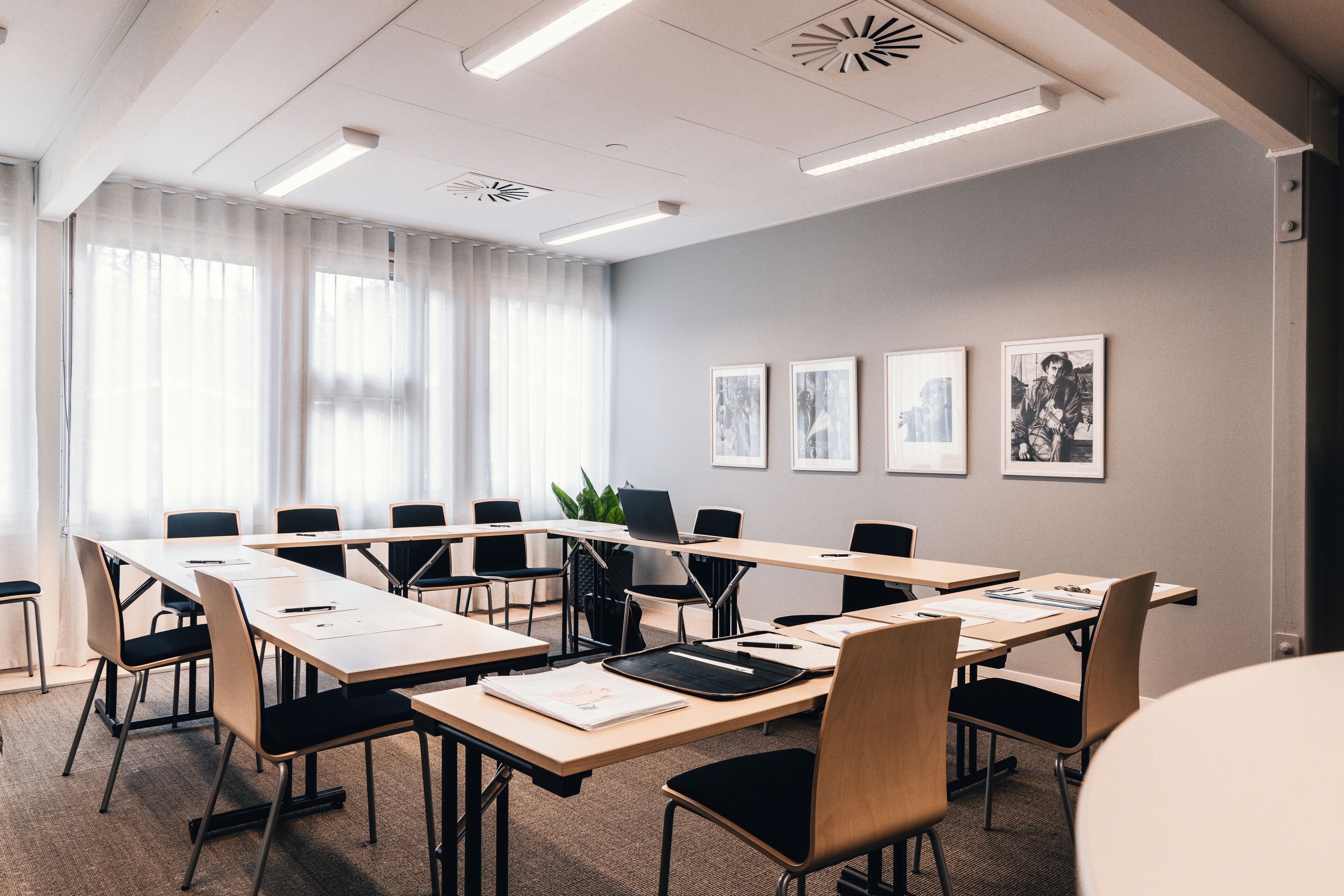 Een congreszaal met lange tafels, stoelen en ingelijste foto's aan de muur.