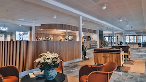 A modern reception area with a wooden reception desk, seating area with orange chairs, and a large screen displaying information. - Ädelfors Hotell och Konferens (Holsbybrunn)