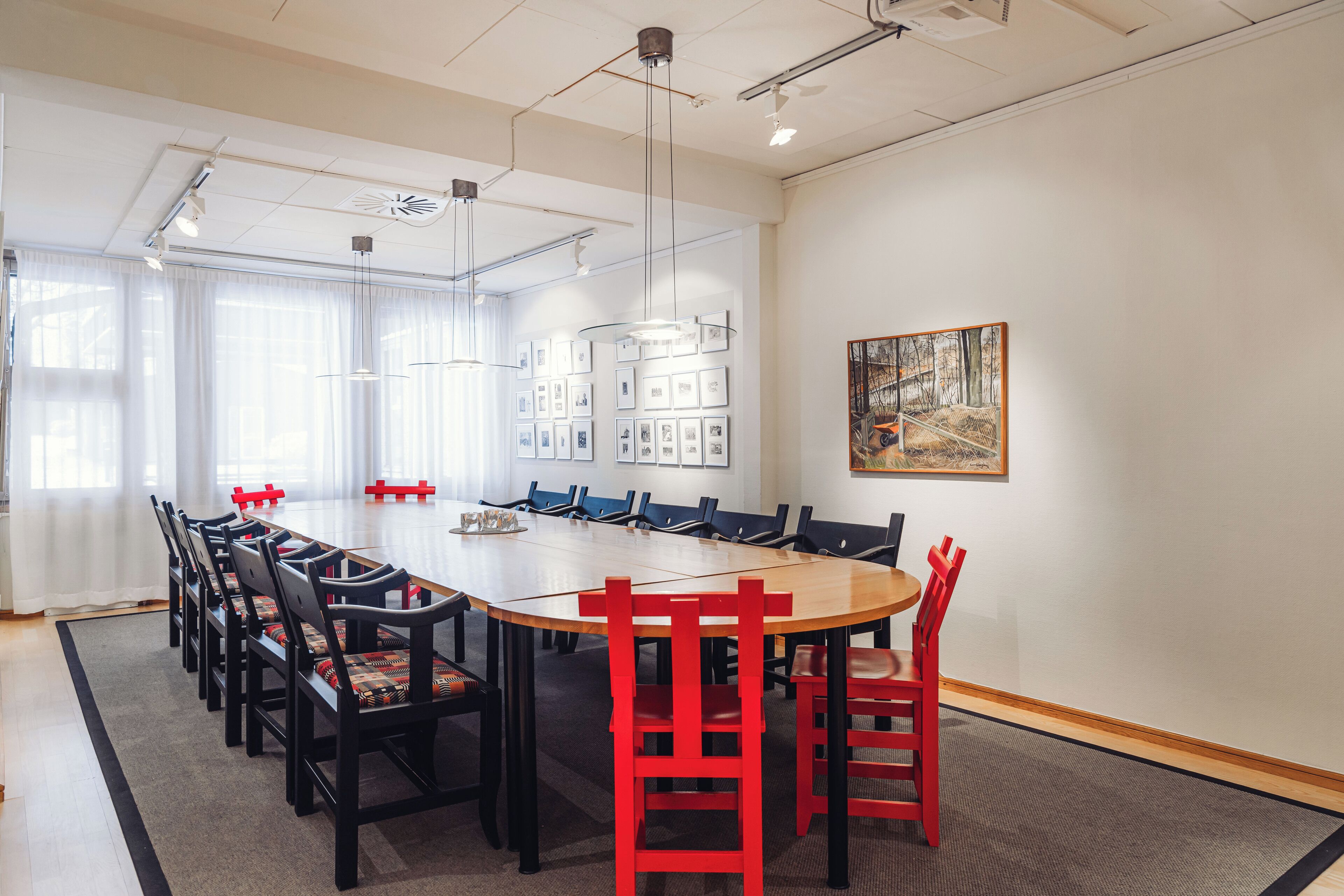 A conference room with a large table, black and red chairs, and framed pictures on the walls.