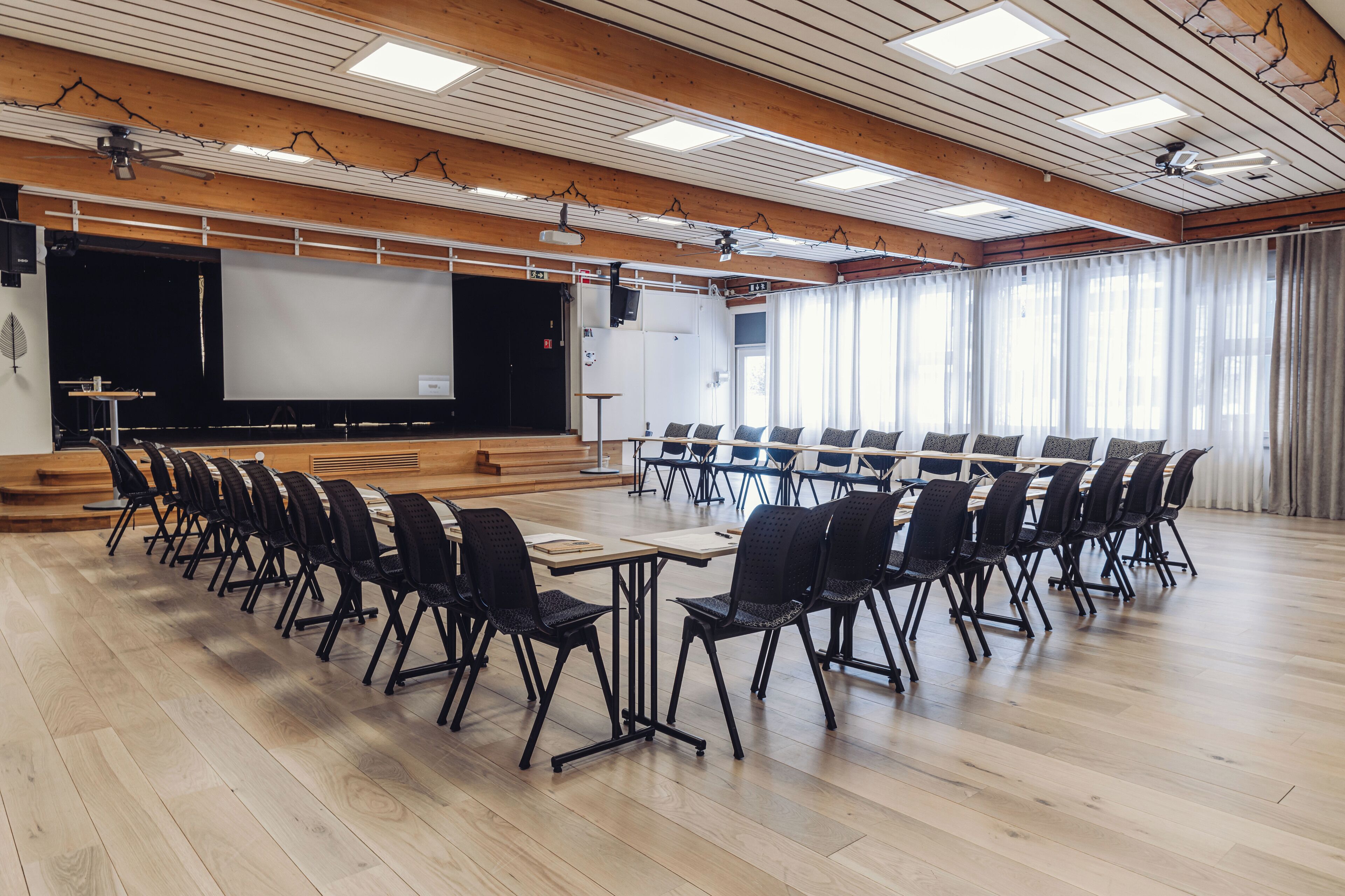 Un salón de conferencias con una larga mesa, sillas, una pantalla de proyector y una pizarra.