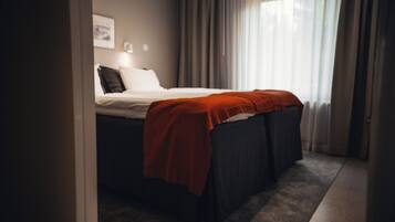 A neatly made bed with a red blanket, a bedside lamp, and a framed picture on the wall.