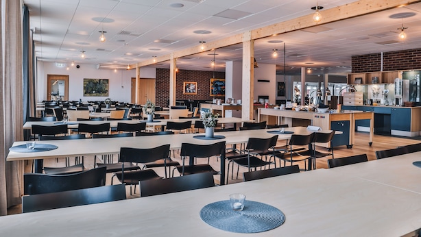 A spacious dining area with multiple tables and chairs, a kitchen area, and a brick wall. - Ädelfors Hotell och Konferens (Holsbybrunn)