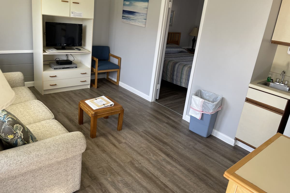 A compact living space with a sofa, a small table, a TV, and a bed in the adjacent room.