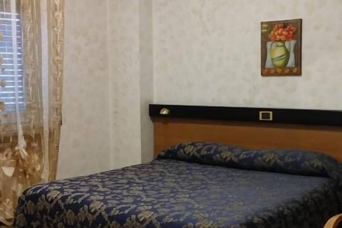 A bedroom with a bed, a headboard, a painting, and a window with curtains.