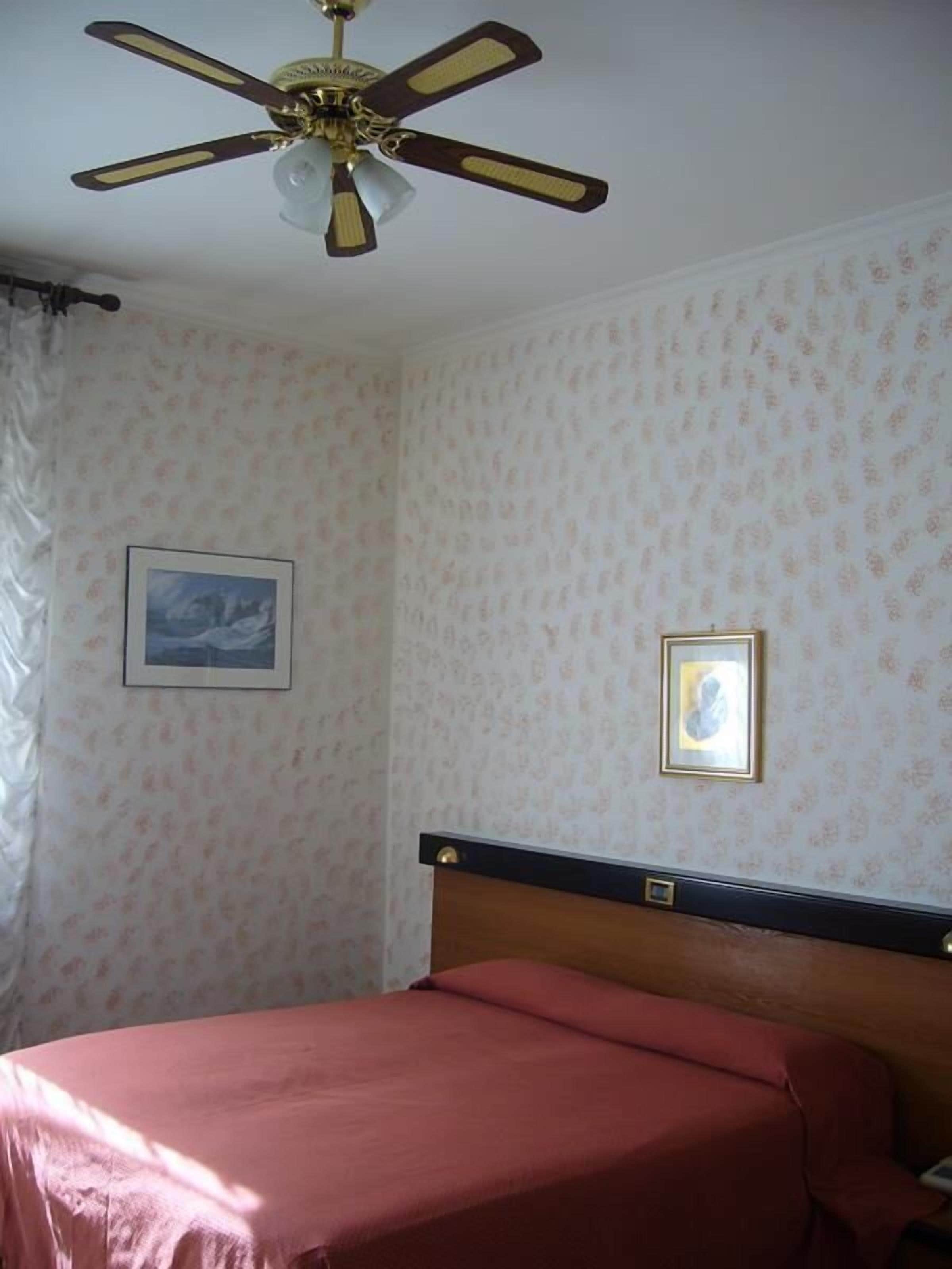 Une chambre à coucher avec un lit, un ventilateur de plafond, un papier peint à motifs floraux et deux tableaux encadrés.