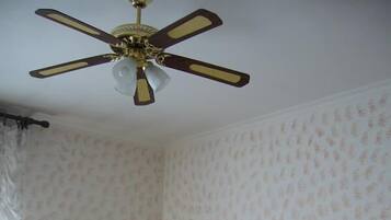 Une chambre à coucher avec un lit, un ventilateur de plafond, un papier peint à motifs floraux et deux tableaux encadrés.