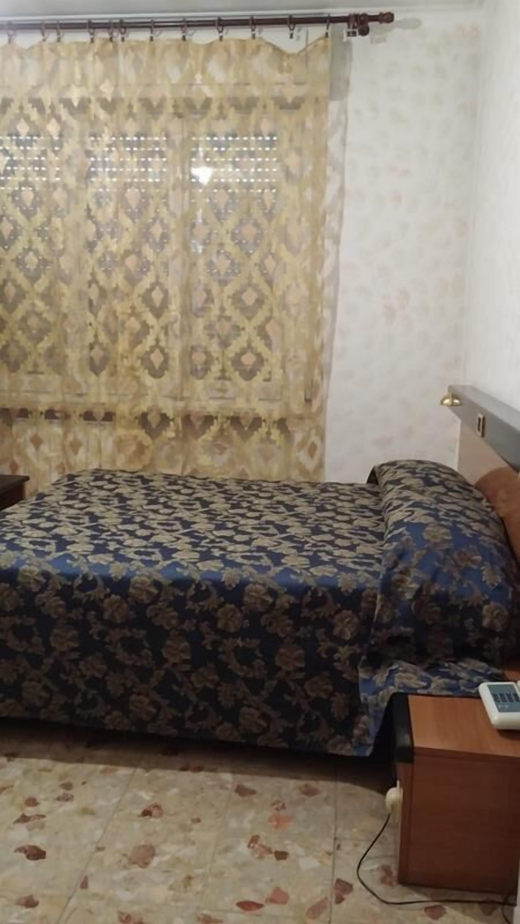 A room with a bed, a nightstand, and a patterned curtain.