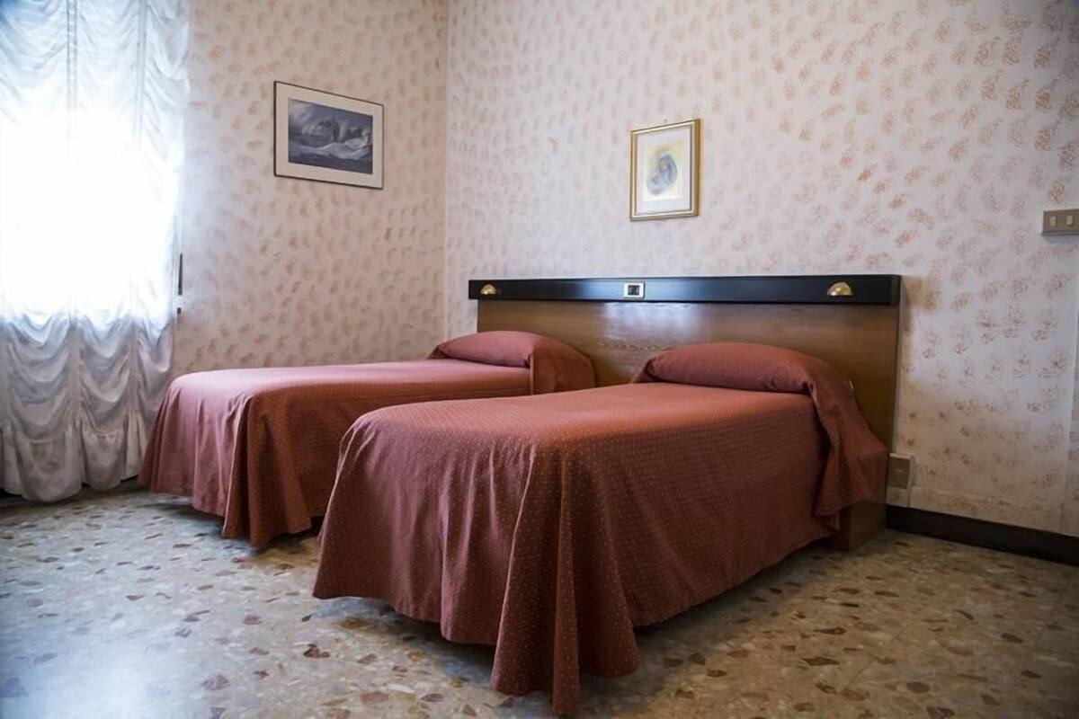 A room with two single beds, a patterned wall, and a window with curtains.