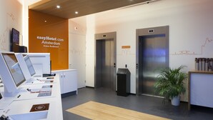 A modern hotel reception area with a digital display, reception desk, elevators, and a potted plant.