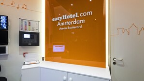 A reception desk with a digital display, a whiteboard, and a sign for easyHotel.com Amsterdam Arena Boulevard.