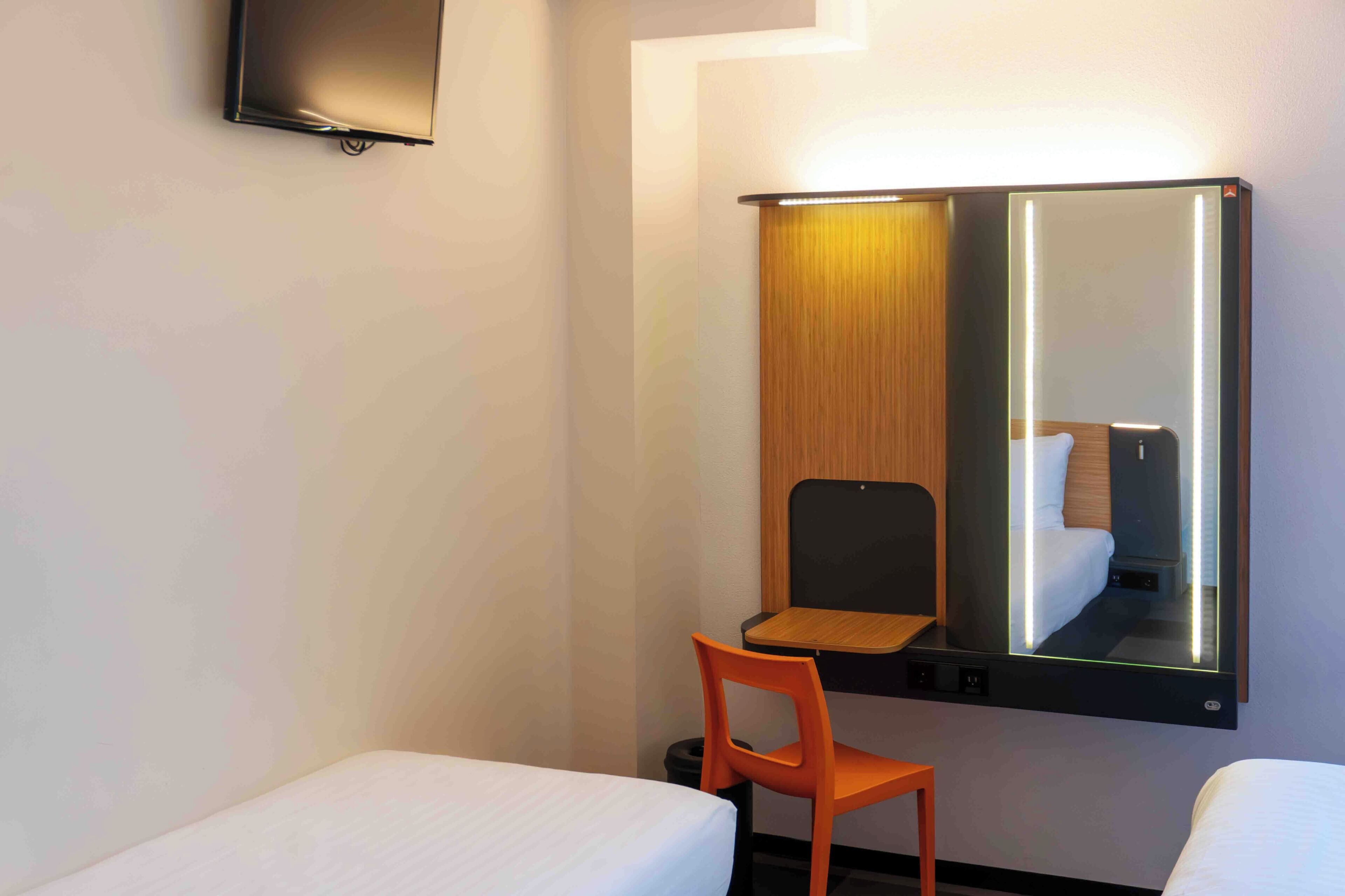 Une chambre d’hôtel avec un lit, une chaise, un bureau, un miroir et un téléviseur.