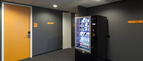 A hallway with a vending machine, a door, and a sign indicating "Rooms 5".