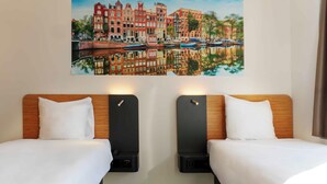 A hotel room with two beds, a painting of a cityscape, and a wooden headboard.