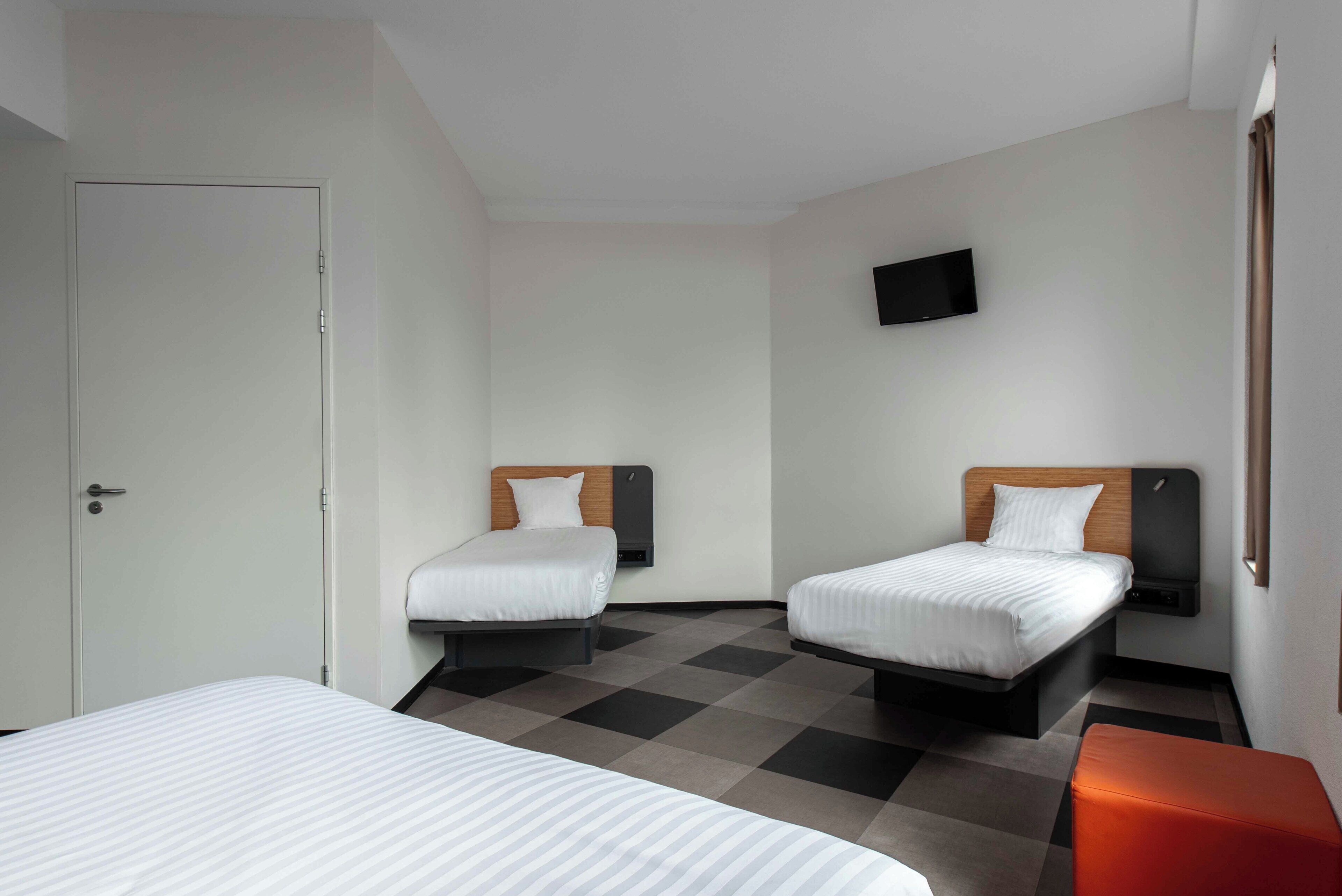 A hotel room with two beds, a door, a flat-screen TV, and a checkered floor.
