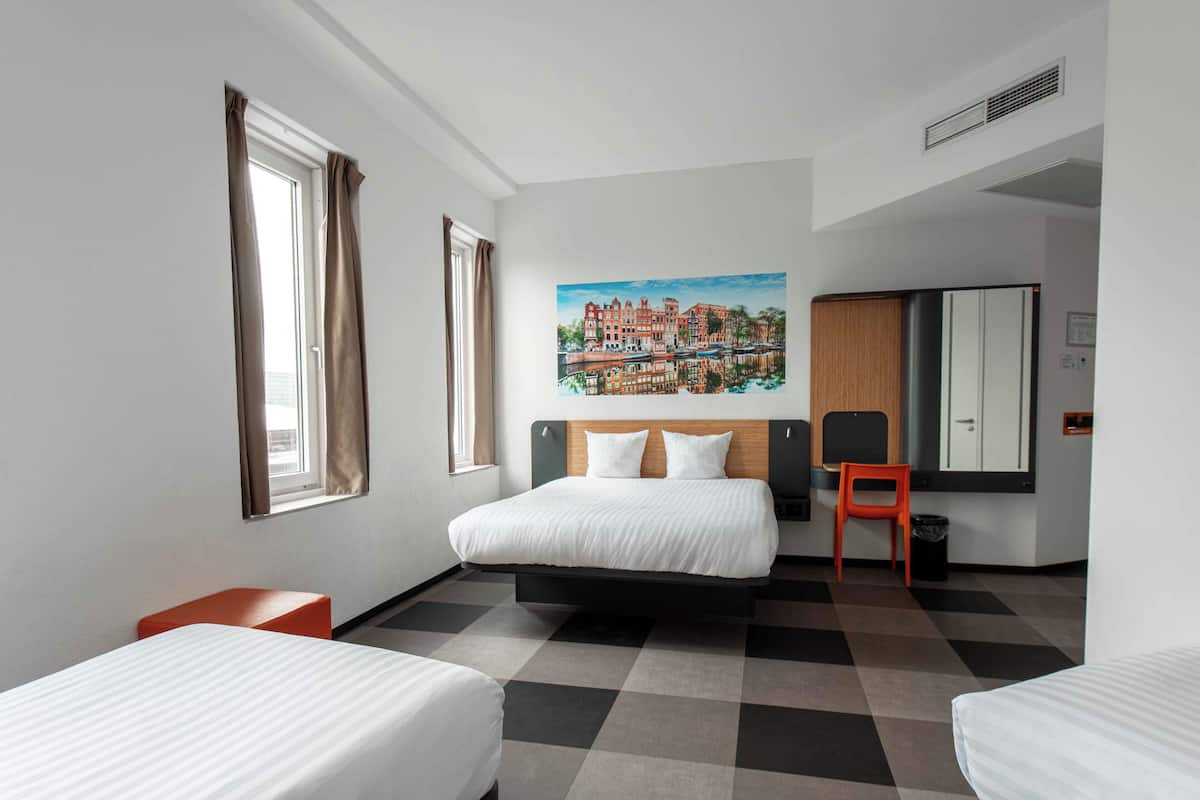 Une chambre d’hôtel comprenant un lit double, deux lits simples, une chaise, un tableau et un miroir.