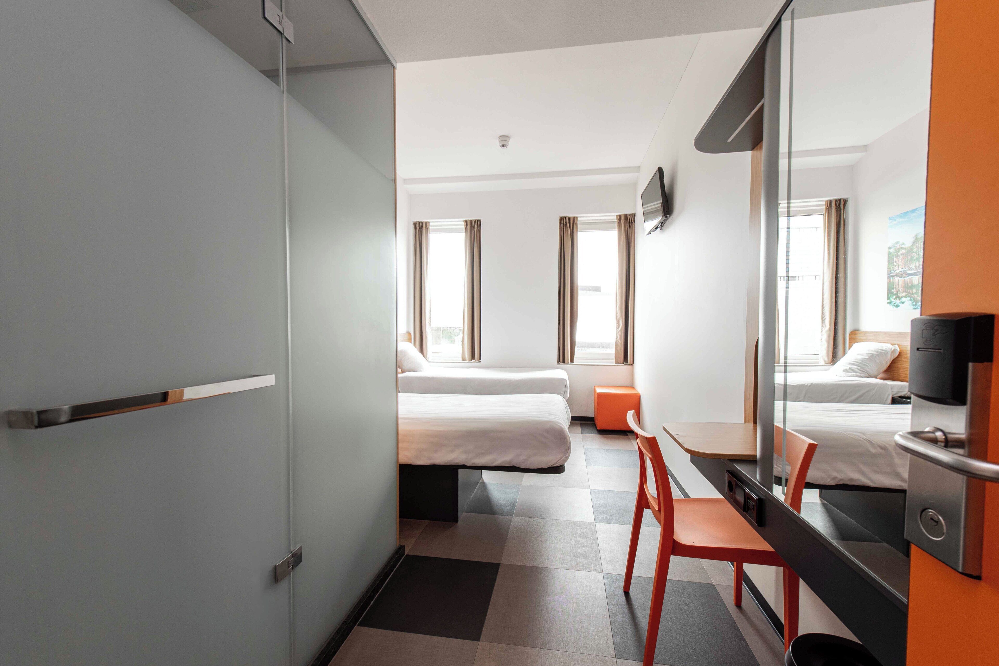 A hotel room with a bed, a desk, a chair, a television, and a window.