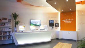 A reception desk with three computer monitors, a plant, and a wall with a cityscape and hotel name.