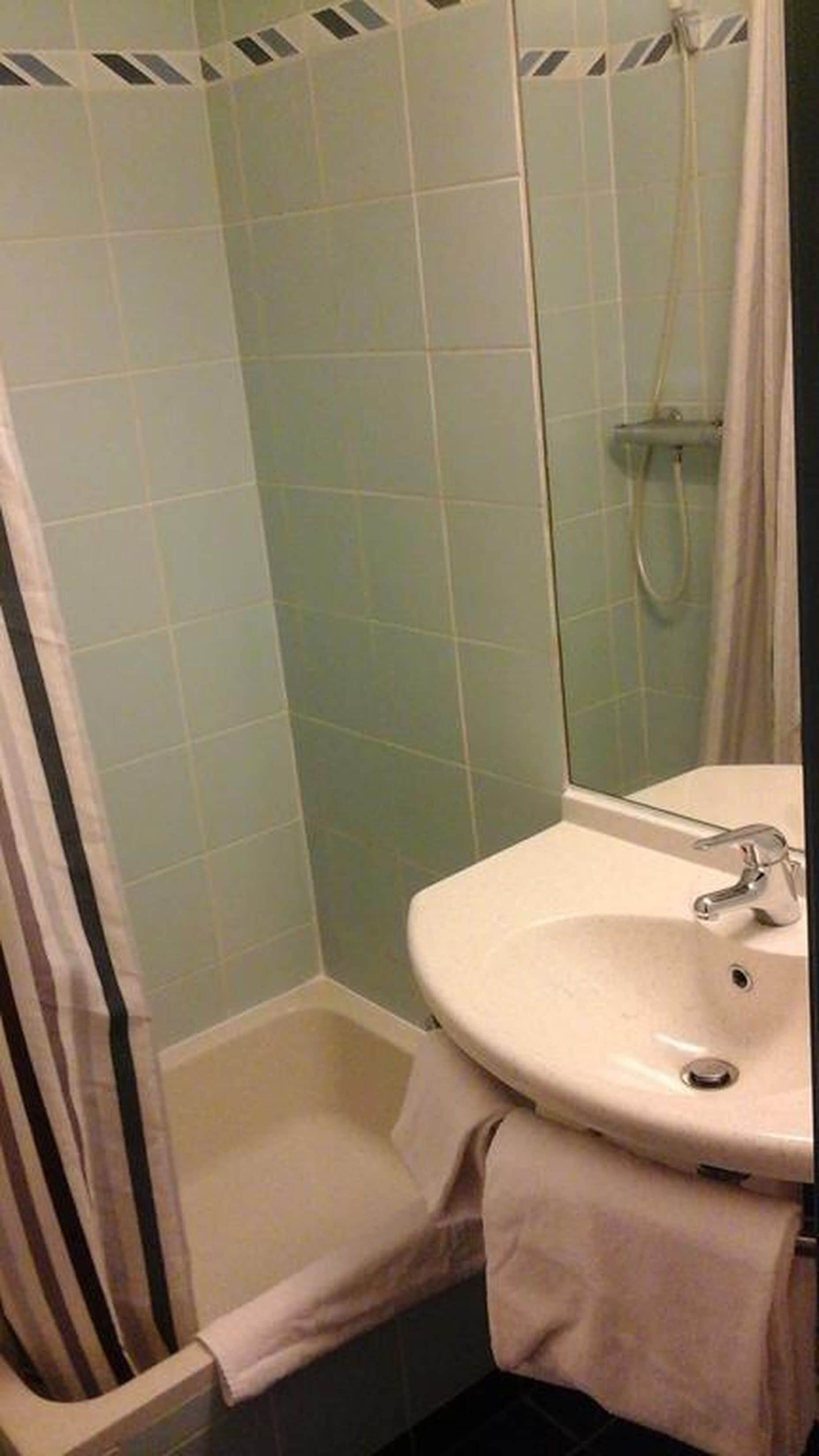 A bathroom with a shower, a sink, and a towel rack.