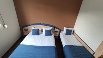 A hotel room with two beds, each with blue and white bedding, and a brown accent wall.
