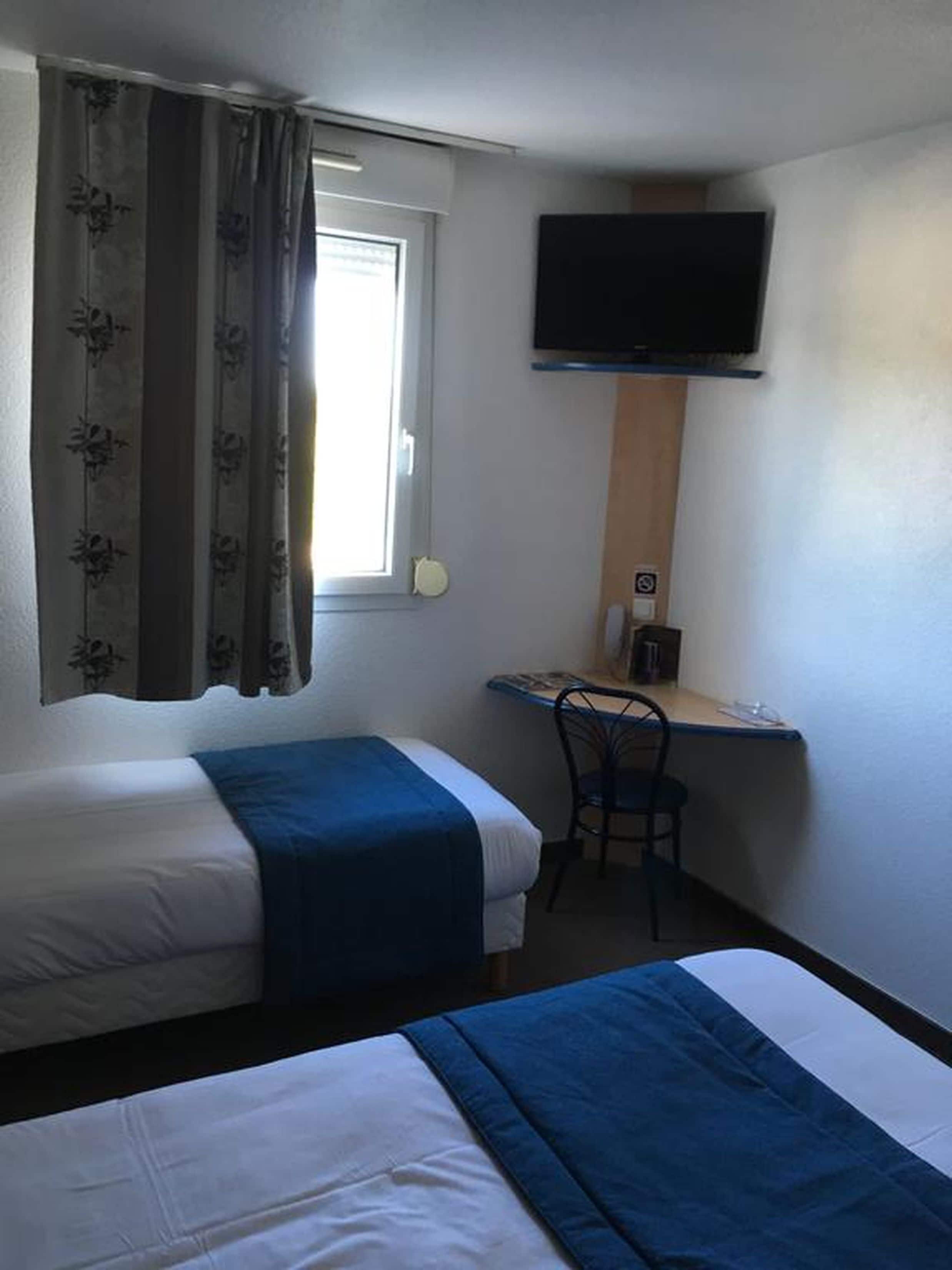 Habitación de hotel con dos camas, un escritorio, una silla, un televisor y una ventana con cortinas.