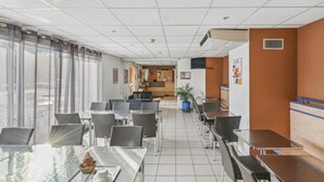 A spacious indoor area with multiple tables and chairs, a reception desk, and a large window with curtains. - Hôtel Akena City Châteaurenard (Chateaurenard)
