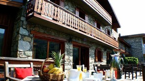 A stone building with a balcony, breakfast table with fruits, cups, and a pitcher. - Hôtel l'Autantic (Bourg-Saint-Maurice)