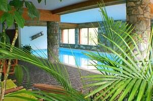 Ein Innenpool mit Steinwänden und Holzbalken, umgeben von tropischen Pflanzen.