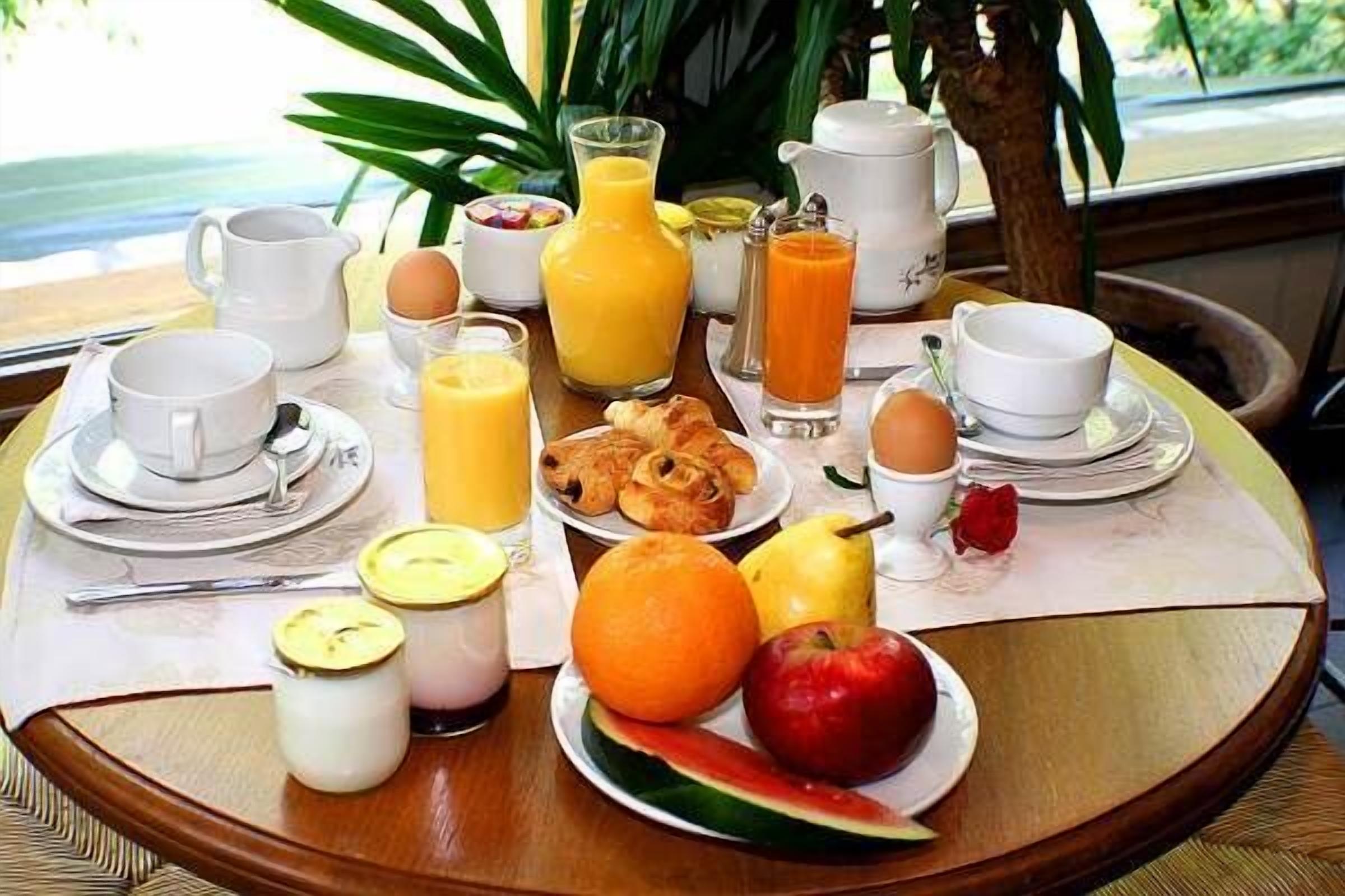 Una mesa de desayuno con diferentes alimentos y bebidas, como huevos, zumo de naranja y bollería.