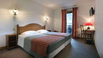 A hotel room with two beds, a desk with a chair, a TV, and a window with curtains.