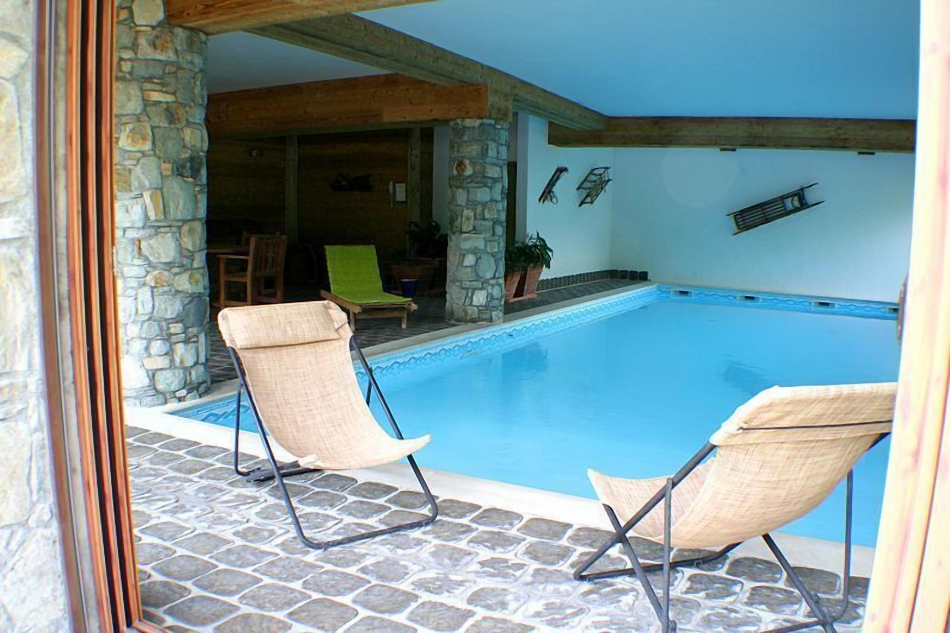 Un área de piscina con dos sillas de descanso, pilares de piedra y suelo de baldosas de piedra.