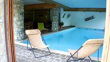 Un área de piscina con dos sillas de descanso, pilares de piedra y suelo de baldosas de piedra.