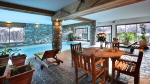 A stone-clad patio with a pool, wooden furniture, and large windows offering views of the outdoors. - Hôtel l'Autantic (Bourg-Saint-Maurice)