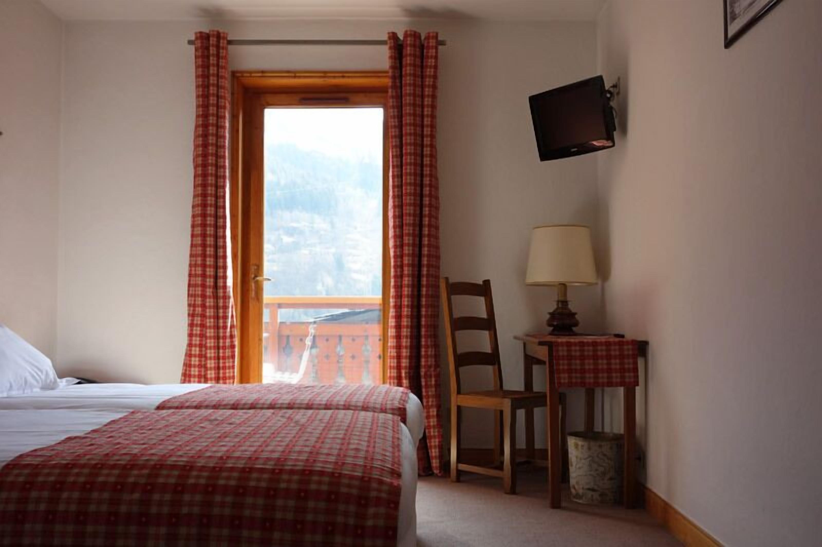 Habitación de hotel con cama, una silla, una mesa con lámpara y televisor en la pared.