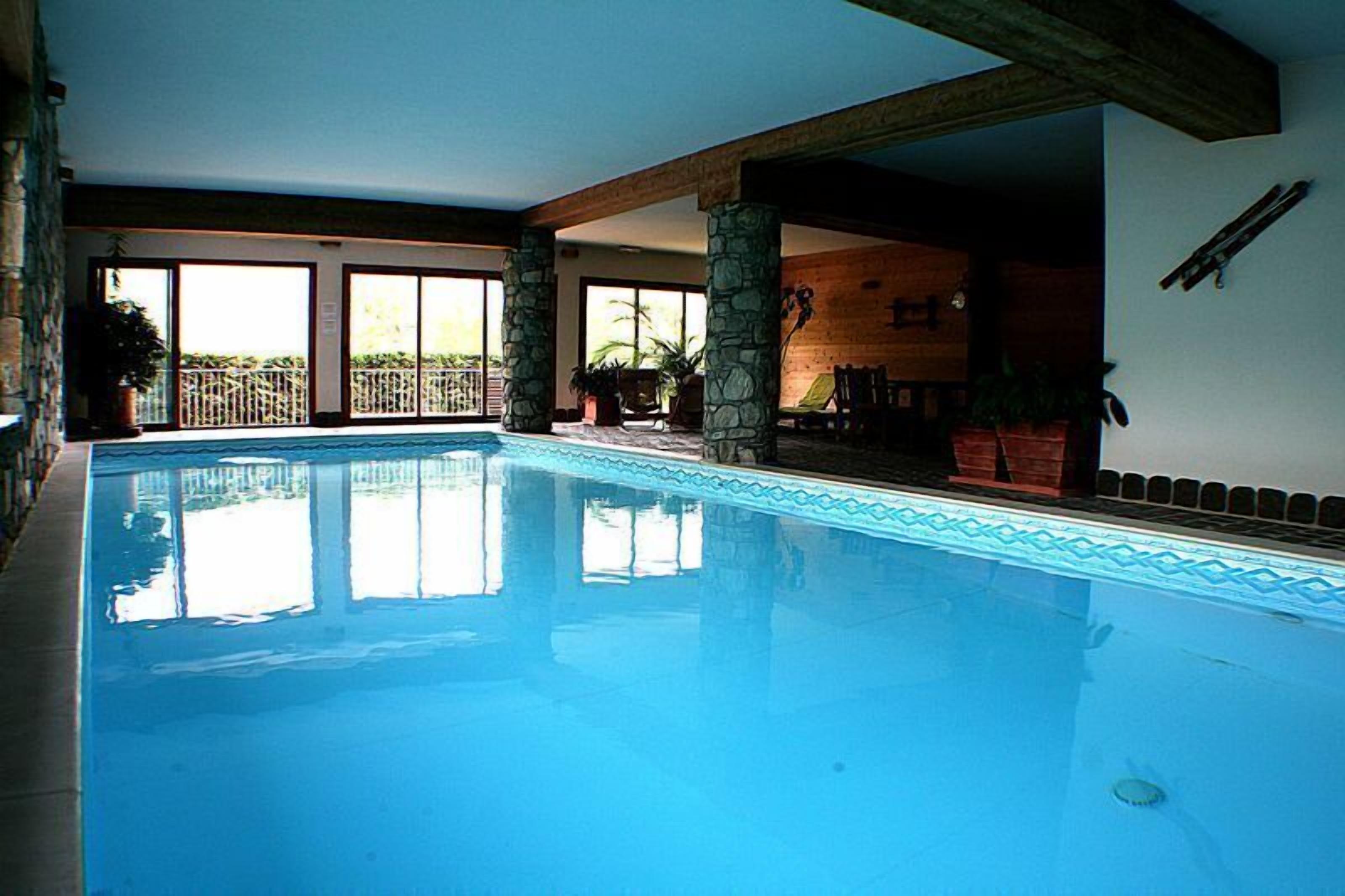 Une piscine intérieure dotée de piliers en pierre, de grandes fenêtres et offrant une vue sur l’extérieur.