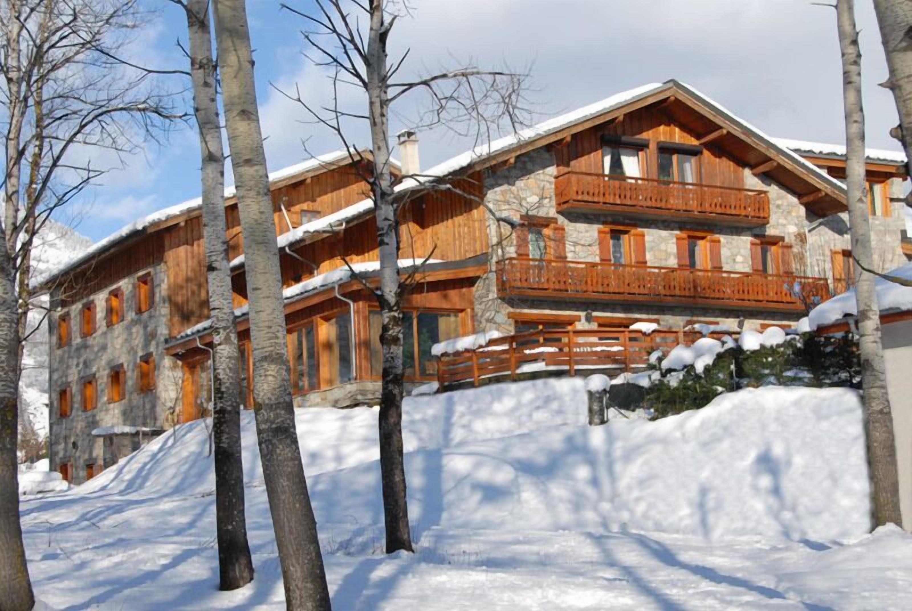 Een houten chalet met meerdere balkons en een gevel van natuursteen, omgeven door sneeuwbedekte bomen.