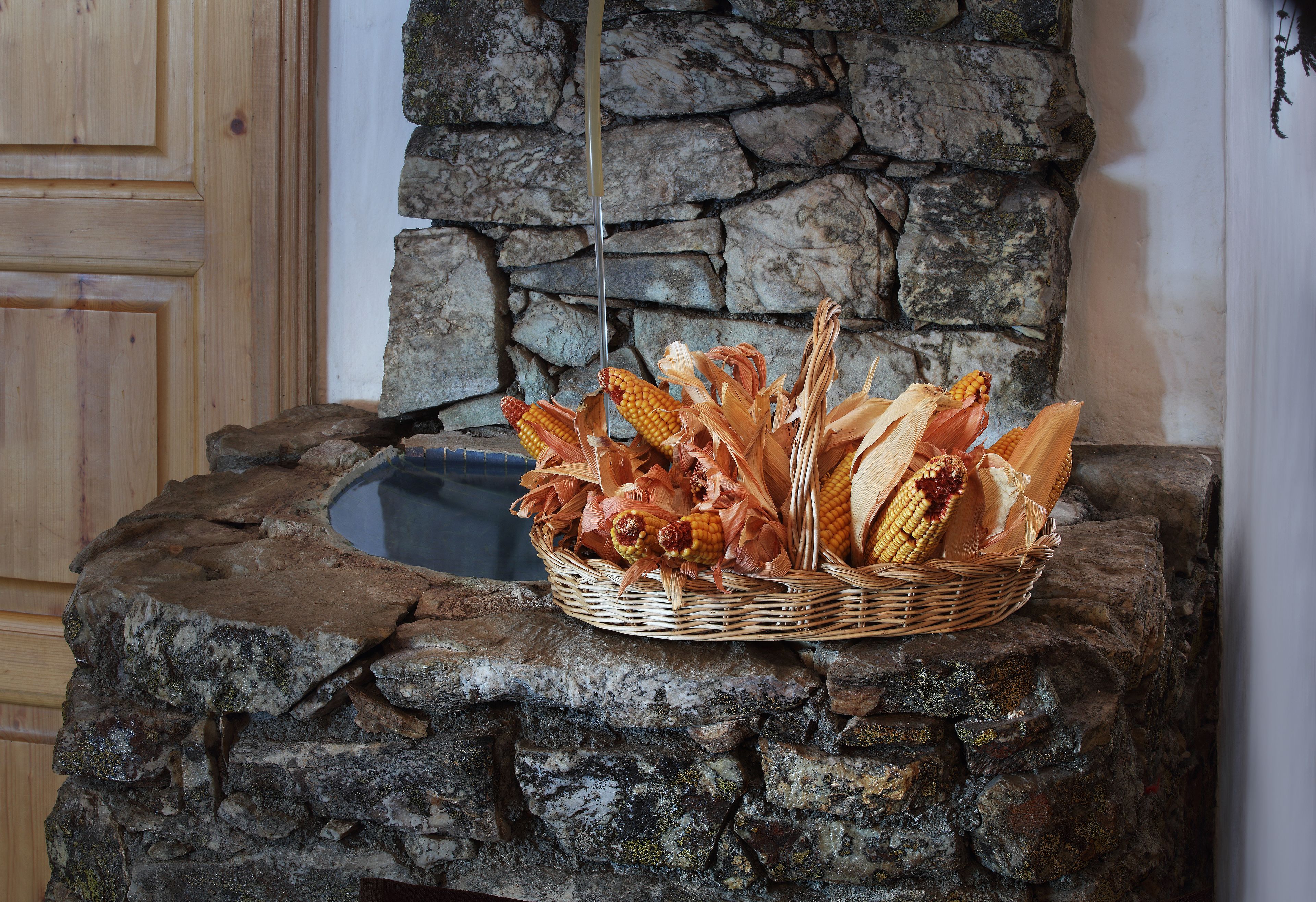 A stone wall with a basket of corn cobs and ears on a wooden ledge.