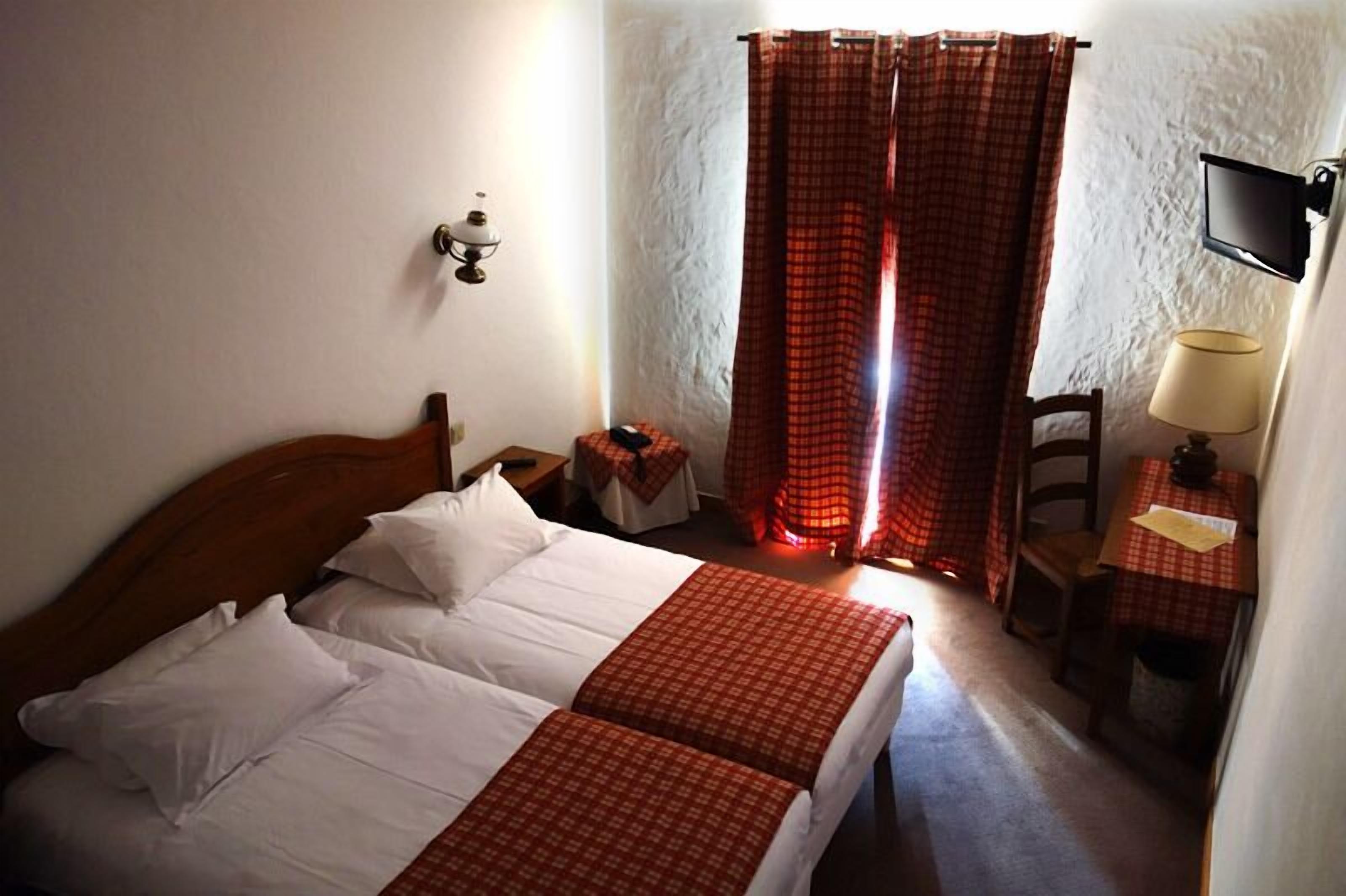 Una habitación de hotel con una cama de madera, una mesita de noche, una mesa con una lámpara y un televisor fijado a la pared.